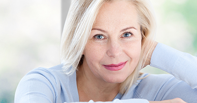 Active beautiful middle-aged woman smiling friendly and looking in camera near window at home. Woman's face closeup. Selective focus.